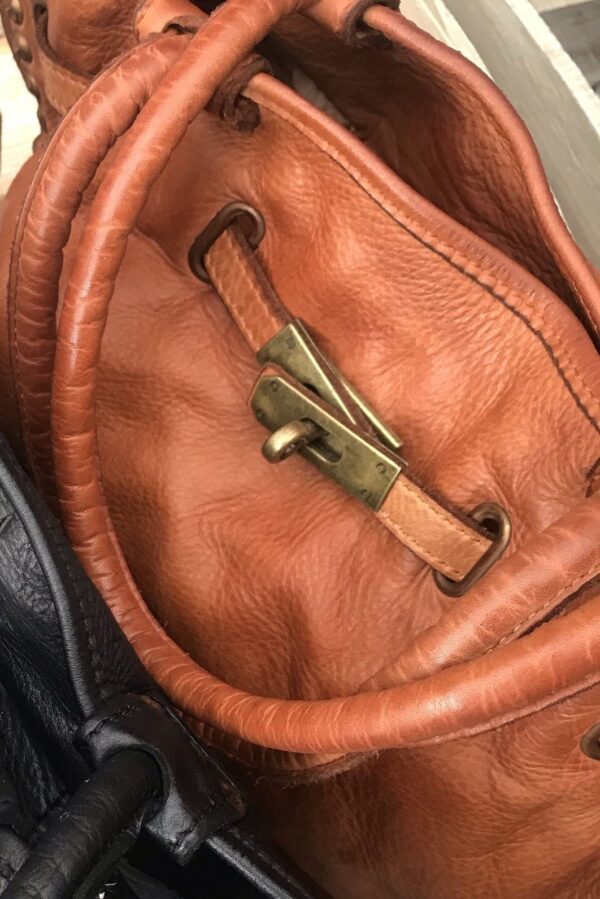 detalle de las tiras de piel decorativas con botón giratorio del bolso de piel lavada camel