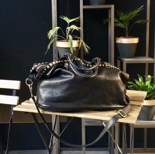 Bolso shopper de piel italiano con decoración de tachas doradas, vista lifestyle sobre la mesa de un restaurante