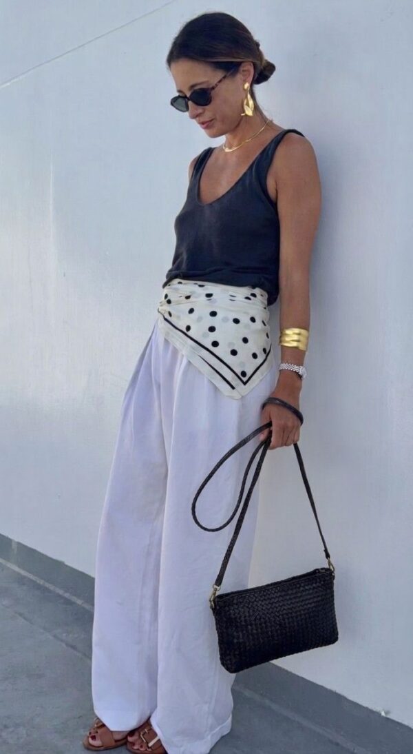 modelo llevando el pochette trenzado hecho a mano en color negro cogido del asa larga extraíble, con un look casual moderno y relajado