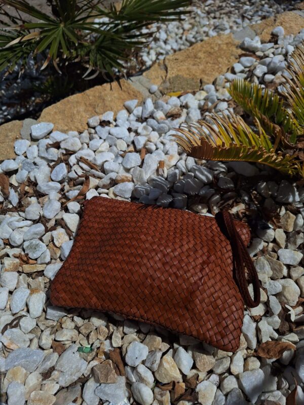Bolso de mano trenzado vista lifestyle en la playa sobre un suelo con piedras blancas