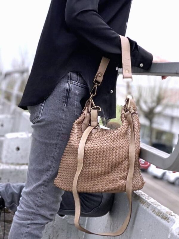 modelo portando el bolso de piel trenzada en su antebrazo con un look urbano en una terraza