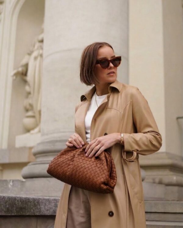 Bolso pouch icónico trenzado con modelo portando el bolso en su mano con un look elegante en tonos camel