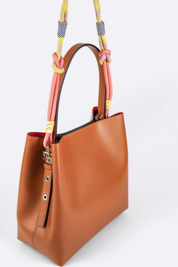bolso bombonera de hombro de piel suspendido en el aire con un asa de nudos multicolor decorativa y detalle del asa en piel con ojales metálicos regulables