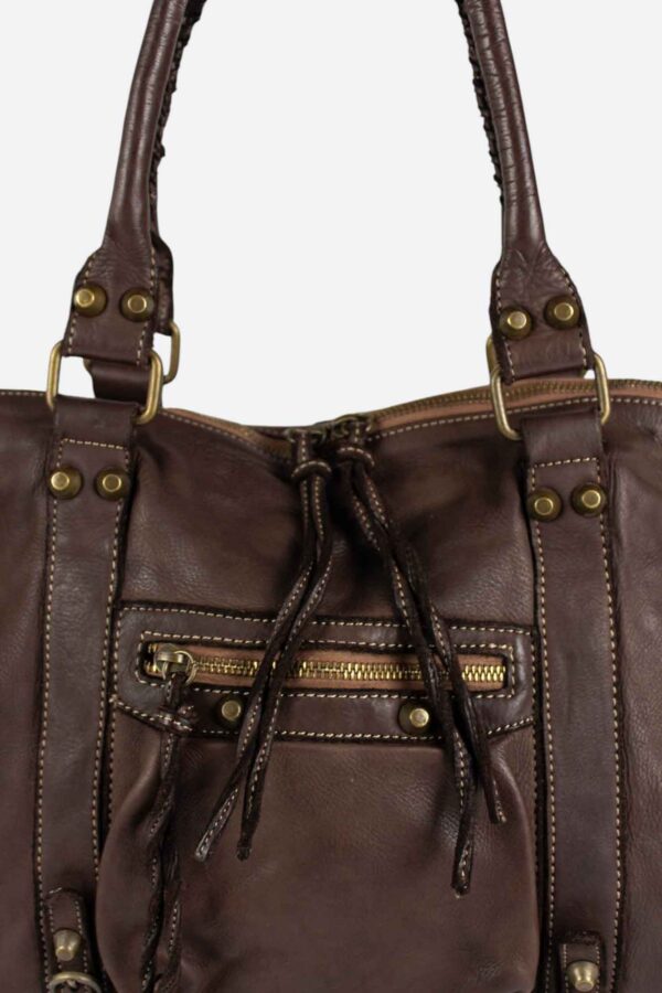 detalle de cerca del bolsillo frontal con cremallera y los cordones de piel del tirador de la cremallera del Bolso estilo motero de piel color chocolate, de máxima tendencia