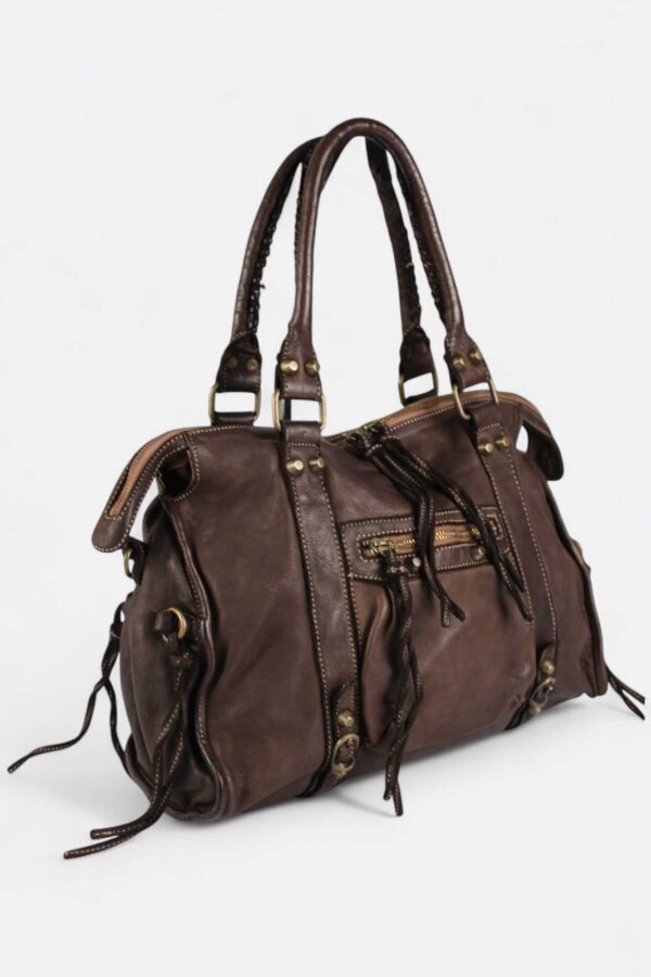 vista lateral del Bolso estilo motero de piel color marrón chocolate con detalle de las 2 asas cortas y cordones decorativos laterales en piel al tono