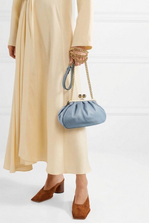 Una modelo lleva el Bolso Carrie Azul Celeste con cierre de bolas doradas y cadenas, completando un estilo vintage con vestido beige y mules marrones