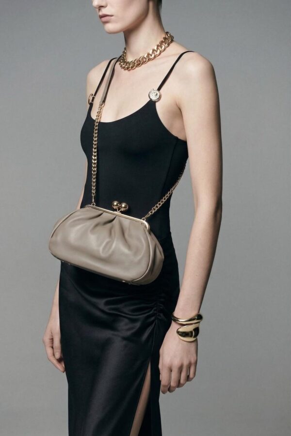 Clutch de piel lisa de ternera con cierre metálico de bolas con modelo llevando el bolso cruzado al hombro
