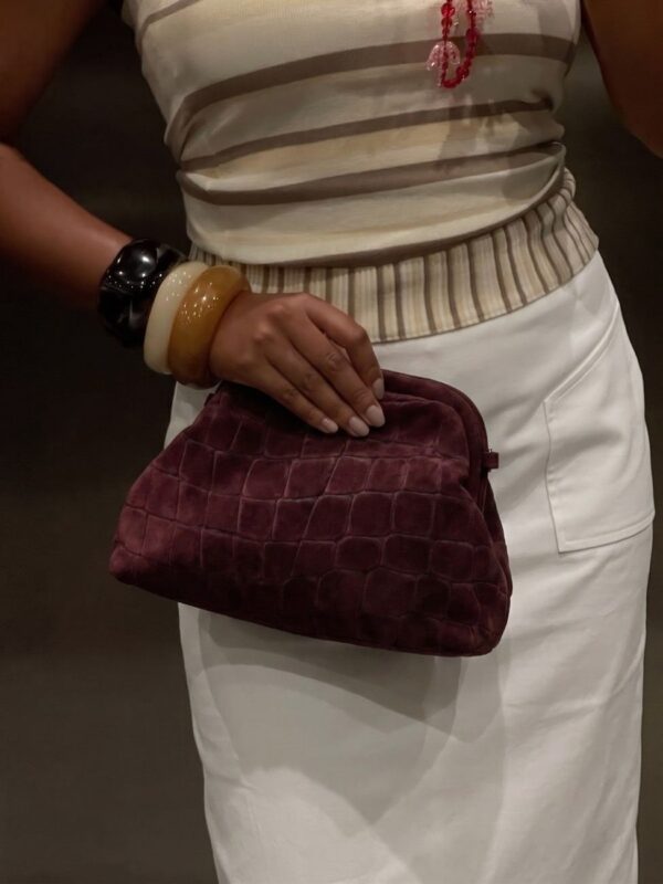 Modelo llevando el bolso pouch de ante burdeos efecto cocodrilo con cierre de boquilla retro con un look urbano en tonos claros