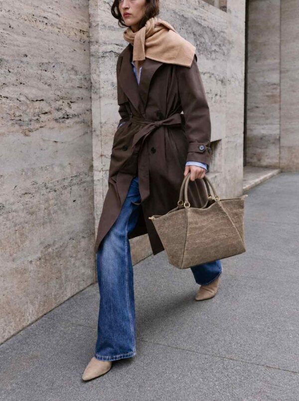Modelo portando el Bolso shopper Arezzo topo de ante con asas cortas de mano. Llevando un look urbano con gabardina